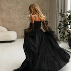Woman in a black evening gown with sheer sleeves in an indoor setting.