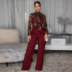 A woman models a two-piece outfit consisting of a long-sleeve high-neck blouse with a leopard print and burgundy panels, paired with matching wide-leg trousers in a burgundy color. She is standing in a modern room with a tufted sofa and a glass side table in the background.