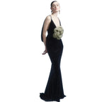 Woman wearing a black evening gown with a floral detail on a plain background