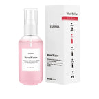 A pink spray bottle of Rose Water Toner resting in water next to its matching white and red retail box.