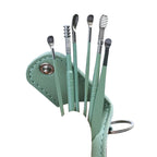 Set of ear cleaning tools in a green case held by a hand against a light blue background