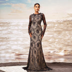Woman in a black lace evening gown standing on a beach with ocean waves in the background