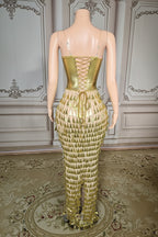 Mannequin wearing a gold, textured evening gown against an ornate wall.