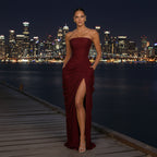 Woman in a burgundy strapless gown with a high slit standing on a wooden pier during sunset.