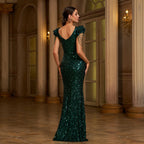 Woman in a green sequin gown standing in an elegant interior setting
