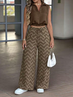 A woman models a two-piece clothing set featuring a brown sleeveless collared crop top and matching wide-leg pants with a brown and beige chevron pattern, styled with white sneakers and a white handbag.