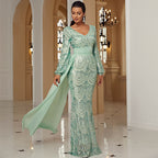 Woman in a green evening gown standing in an elegant hallway.