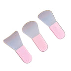 Three small spatulas with pink and clear ends on a wooden and gray surface.