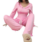 A woman wearing a pink two-piece lounge set with a long-sleeve top featuring a ruffled neckline and matching drawstring pants, posed against a plain white background.