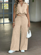 Woman wearing a beige sleeveless top and patterned wide-leg pants, holding a white handbag.