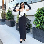 Woman in a black dress with white floral accessories posing outdoors.