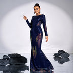 Woman in a long, dark blue evening gown with intricate patterns standing against a white background.