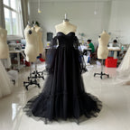 Black evening gown on a mannequin in a room with other mannequins and people working.