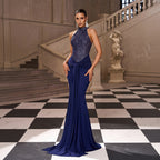 Woman in a blue evening gown standing in an elegant interior setting with checkered floor and staircase.