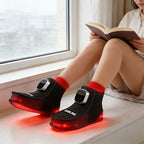 Person wearing black and red massage shoes with glowing red lights, sitting by a window reading a book.